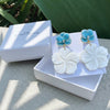 Jewelry set with white and blue earrings in a white box on a stone surface.