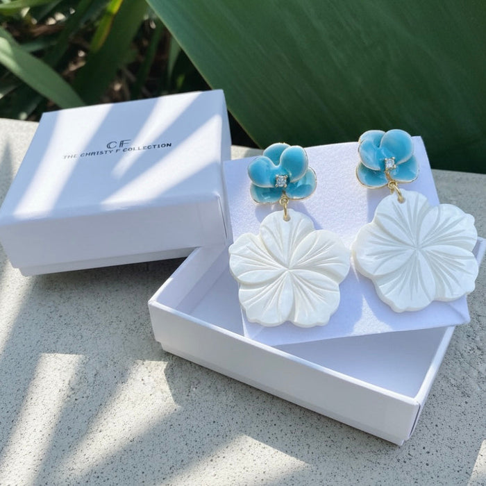 Jewelry set with white and blue earrings in a white box on a stone surface.
