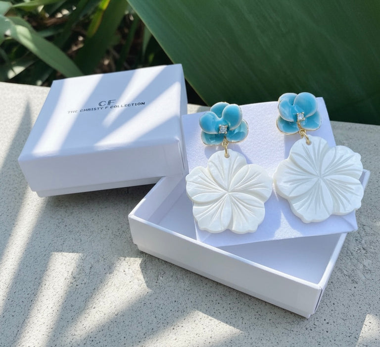 Jewelry set with white and blue earrings in a white box on a stone surface.