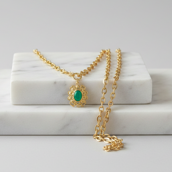 Gold necklace with a green pendant on a marble surface