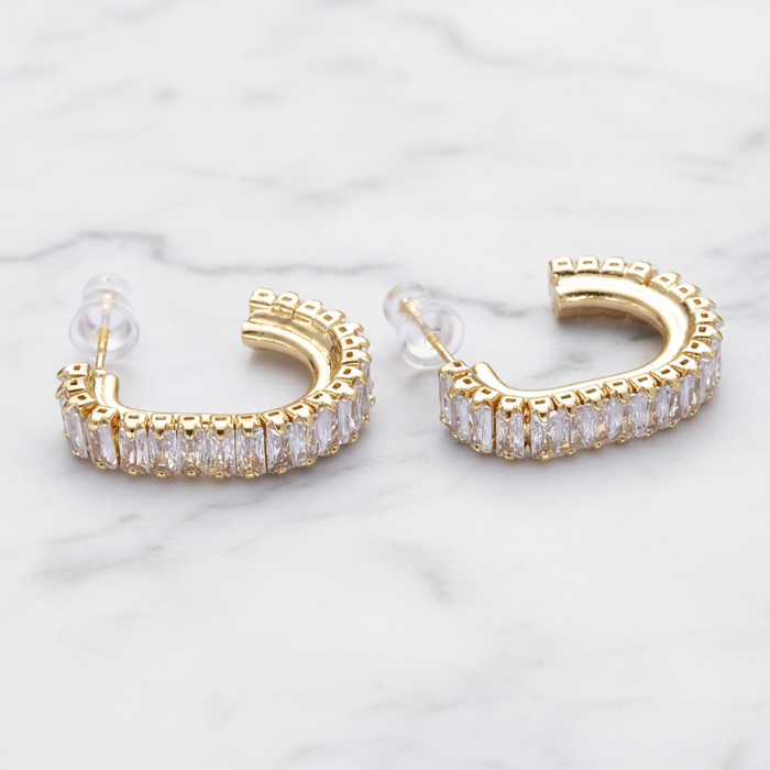 Gold hoop earrings with clear gemstones on a light marble background