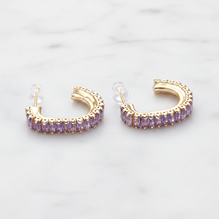 Gold hoop earrings with purple stones on a light gray background