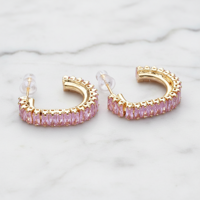 Gold hoop earrings with pink gemstones on a marble surface