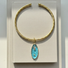 Gold necklace with a blue pendant on a textured beige card