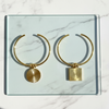 Gold hoop earrings with circular and square pendants on a marble surface