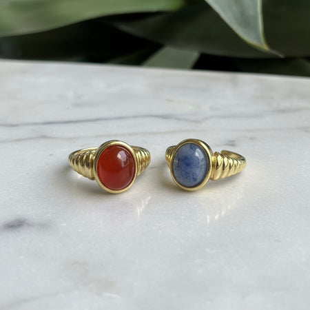 Two gold rings with gemstones on a marble surface