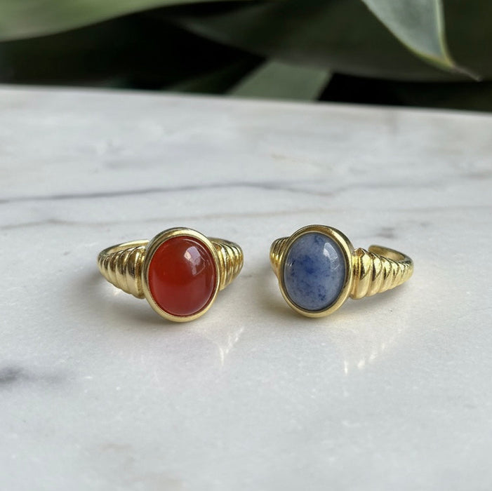 Two gold rings with gemstones on a marble surface