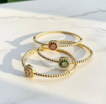 Gold bracelets with colorful charms on a light surface