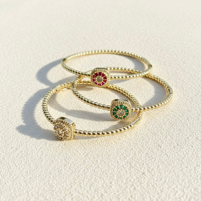 Set of gold bracelets with gemstone charms on a light background