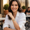 Woman sitting outdoors at a cafe, wearing a white shirt and gold bracelet.