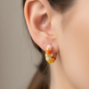 Close-up of an ear wearing a gold and orange hoop earring with a blurred background