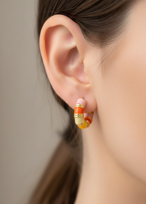 Close-up of an ear wearing a gold and orange hoop earring with a blurred background