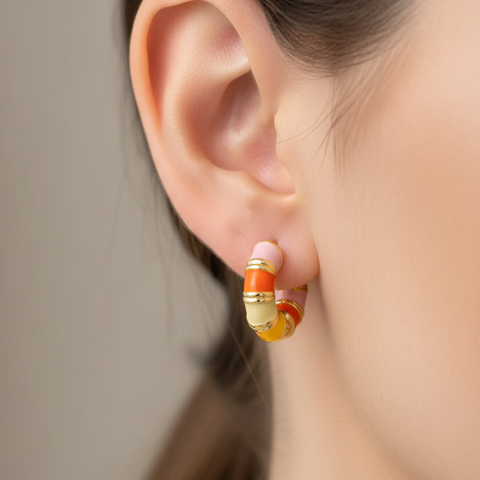 Close-up of an ear wearing a gold and orange hoop earring with a blurred background