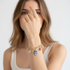 Woman wearing a gold bracelet with colorful charms on a plain background