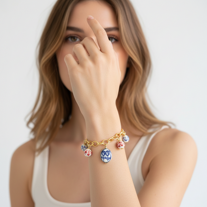Woman wearing a gold bracelet with colorful charms on a plain background
