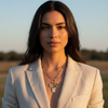 Woman wearing a light-colored blazer and multiple necklaces outdoors with a blurred background