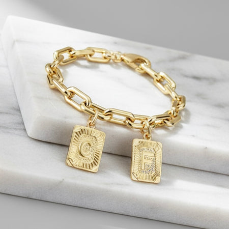Gold chain bracelet with square charms on a marble surface