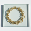 Gold bracelet on a clear display card with a white background