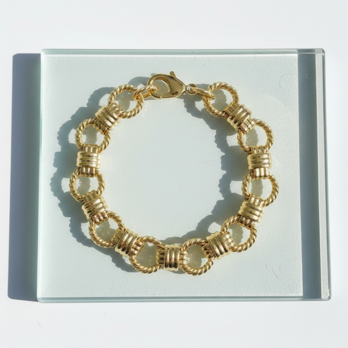 Gold bracelet on a clear display card with a white background