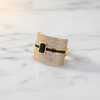Gold ring with black accents on a marble surface
