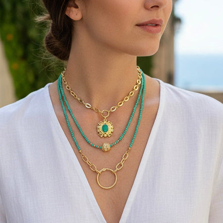 Woman wearing a gold and turquoise necklace with a white top outdoors.