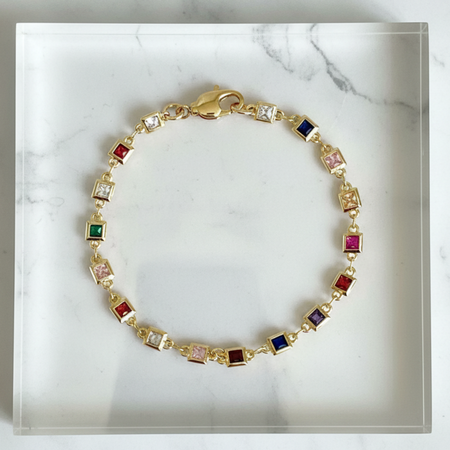 Gold bracelet with colorful gemstones on a marble surface