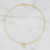 A delicate gold wire choker necklace with a small teardrop crystal pendant, displayed on a white marble background.
