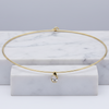 A delicate gold wire bangle necklace with a small teardrop-shaped clear gemstone pendant, displayed on a white marble block against a light gray background.