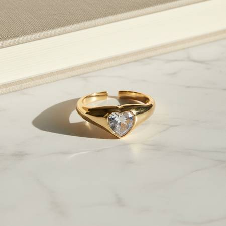 Gold ring with a heart-shaped gemstone on a marble surface