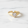 Gold ring with a heart-shaped diamond on a white marble background