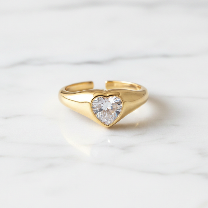 Gold ring with a heart-shaped diamond on a white marble background