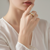 Close-up of a hand wearing a gold ring with a diamond on a neutral background