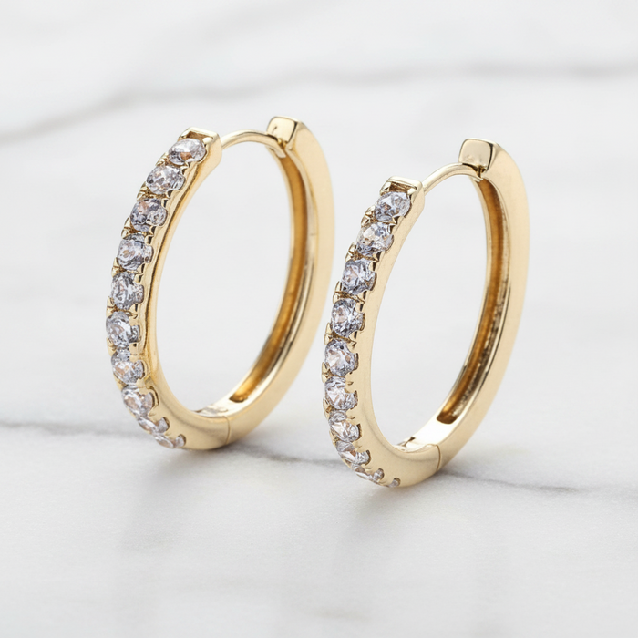 Gold hoop earrings with clear gemstones on a light gray background