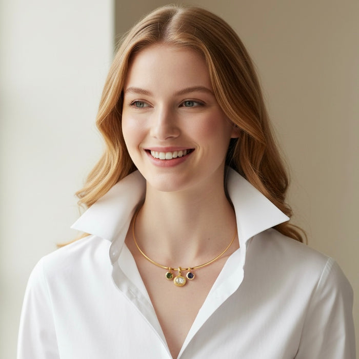 A smiling woman with blonde hair wearing a white collared shirt and a delicate gold necklace with small colorful charms, set against a soft beige background.