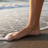 Gold anklet on a foot standing in shallow water at the beach