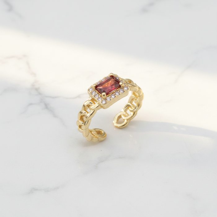 Gold ring with a red gemstone on a light background
