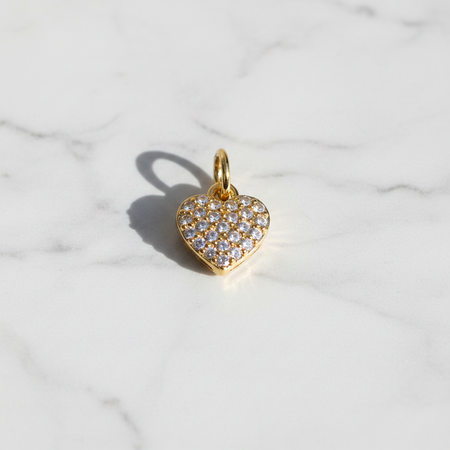 Gold heart-shaped pendant with clear stones on a marble background