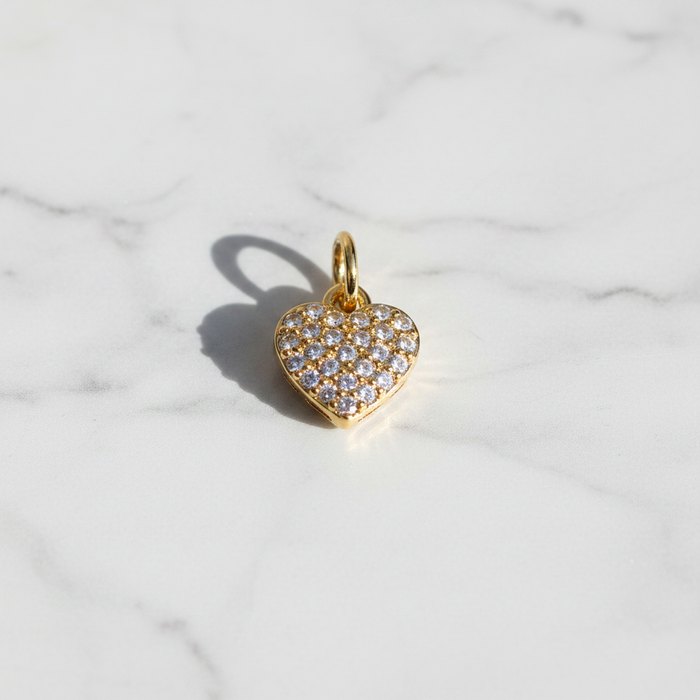 Gold heart-shaped pendant with clear stones on a marble background