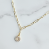Gold necklace with a circular pendant on a marble surface