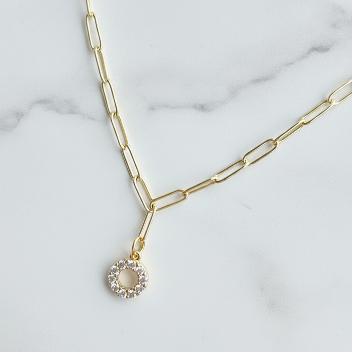 Gold necklace with a circular pendant on a marble surface
