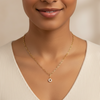 Woman wearing a gold necklace with a small pendant against a neutral background
