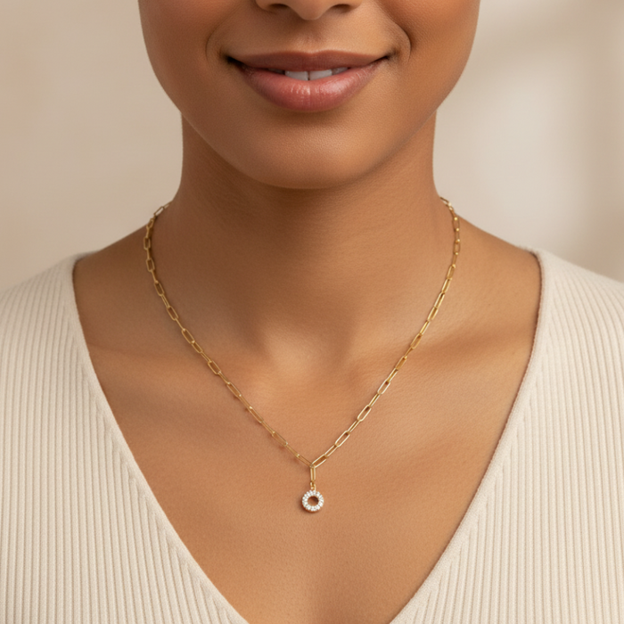 Woman wearing a gold necklace with a small pendant against a neutral background