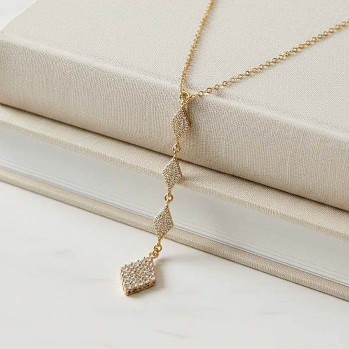 Gold necklace with diamond pendants on a beige surface
