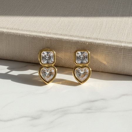 Gold earrings with heart and square cut gemstones on a light fabric background