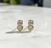 Gold heart-shaped earrings with clear stones on a marble surface