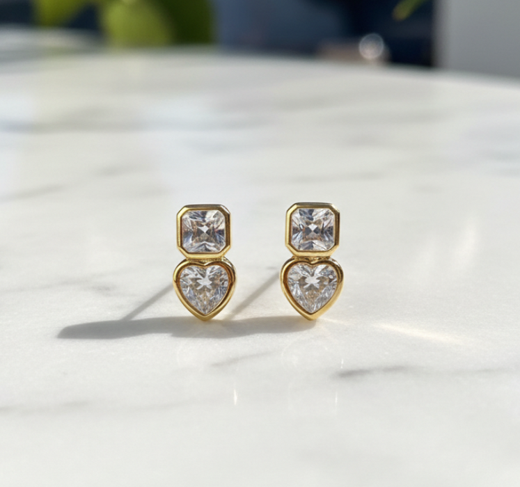 Gold heart-shaped earrings with clear stones on a marble surface