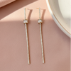 Pair of diamond earrings on a pink surface with a white dish in the background