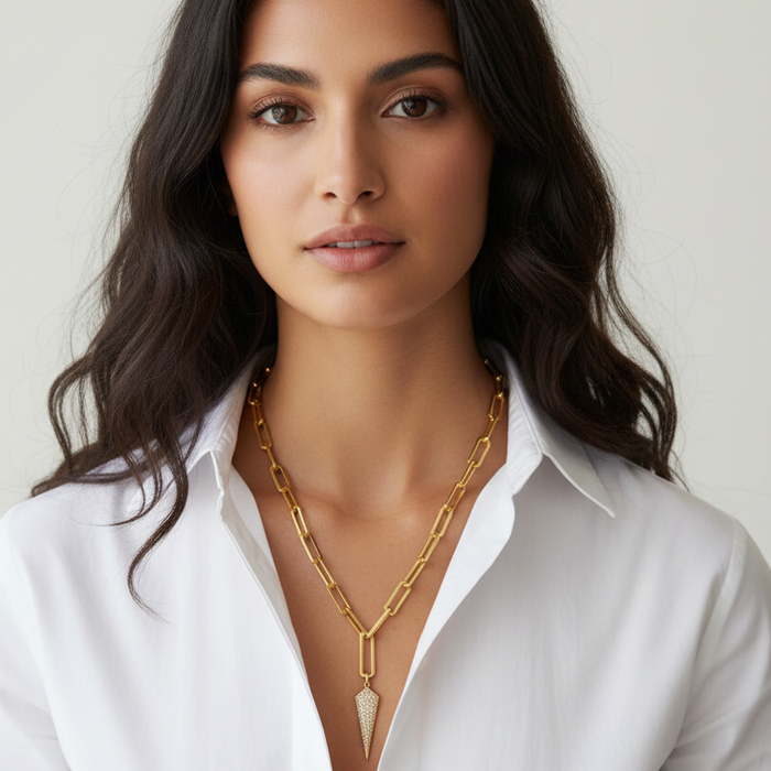 Woman wearing a gold necklace with a white shirt against a plain background