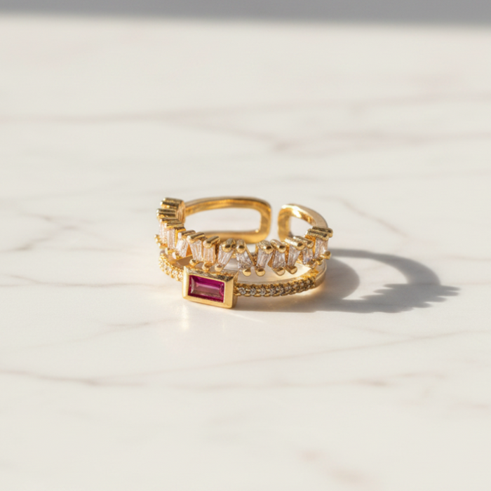 Gold ring with a red gemstone on a light beige surface