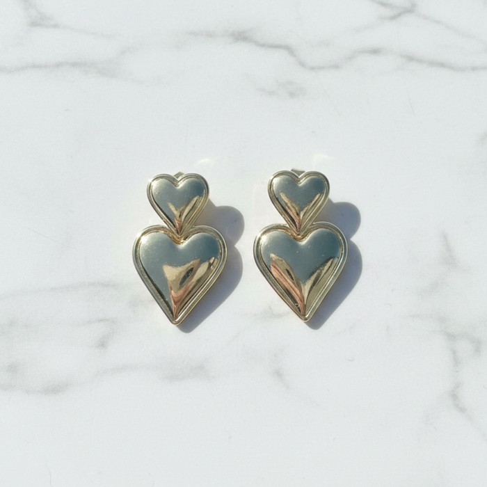 Heart-shaped gold earrings on a light marble background